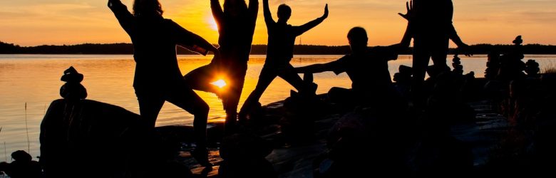 Viisi ihmistä tanssii rannalla kesällä auringonlaskun aikana