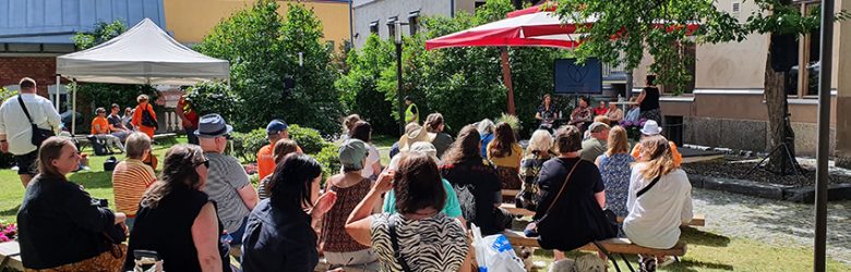 Ihmisiä kesällä ulkona kuuntelemassa keskustelutilaisuutta Porin kaupungintalon pihalla SuomiAreenassa.
